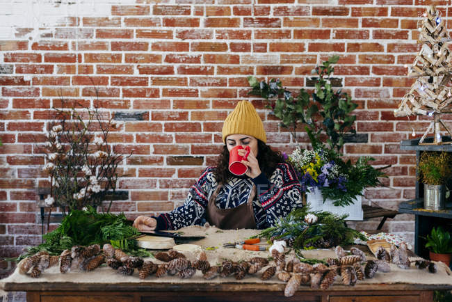 Портрет женщины, пьющей кофе за столом и болтающей на планшете в цветочном ателье — стоковое фото