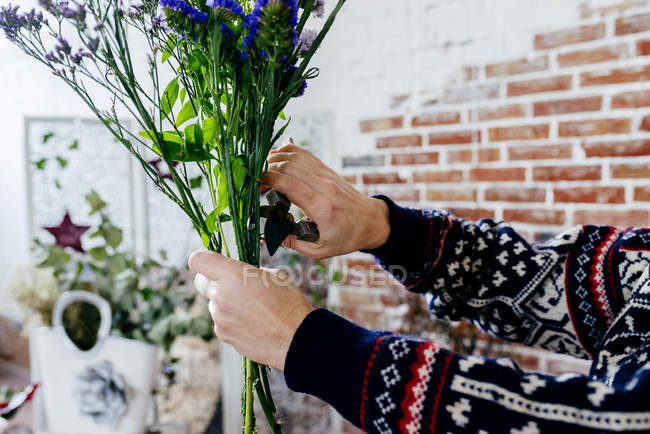 Crop hands in knitted sweater cutting flowers with pruner — Stock Photo