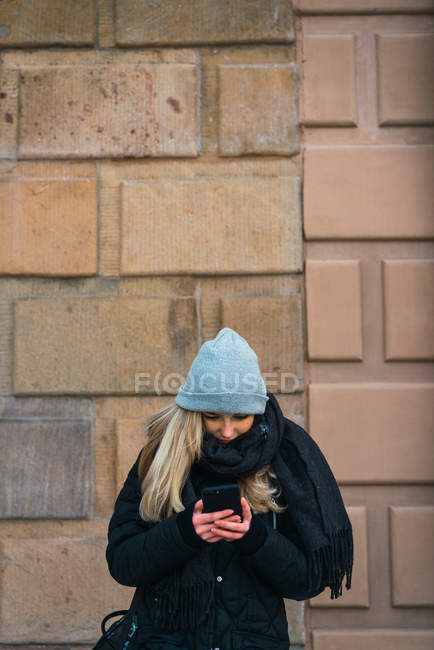 Вид спереду блондинки, використовуючи смартфон на зимовій вулиці — стокове фото