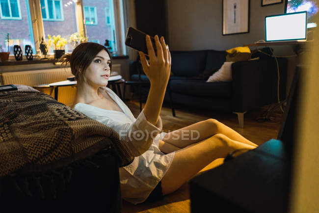 Ritratto di giovane donna sul pavimento di casa e fare selfie su smartphone — Foto stock