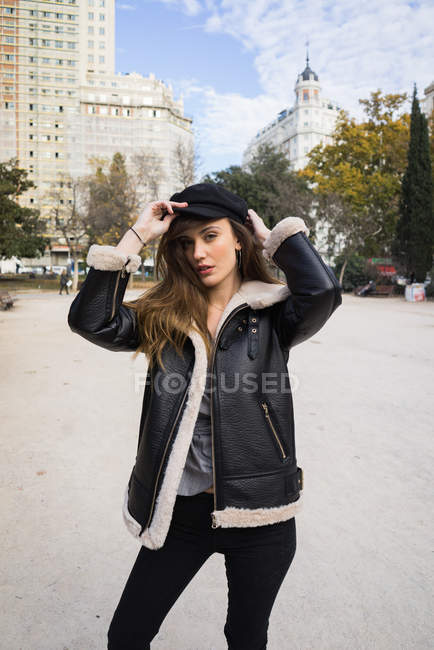Hübsche junge Frau blickt in Kamera und setzt Mütze im Stadtpark auf. — Stockfoto