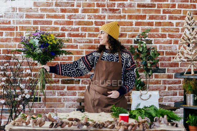 Retrato de florista feminina em avental posando com buquê contra parede de tijolo no fundo — Fotografia de Stock