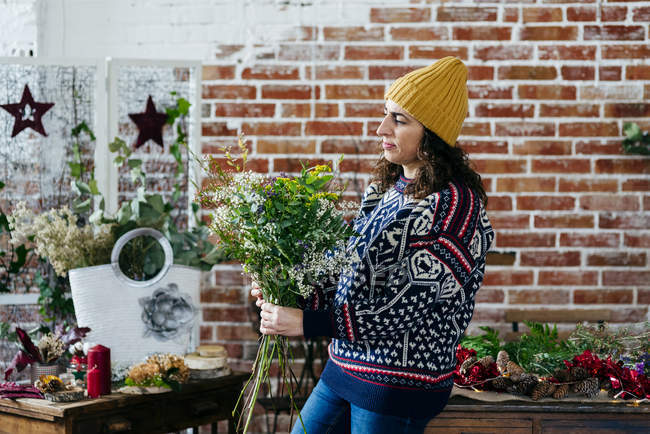 Side view of woman in knitted sweater and hat looking down at bouquet — Stock Photo