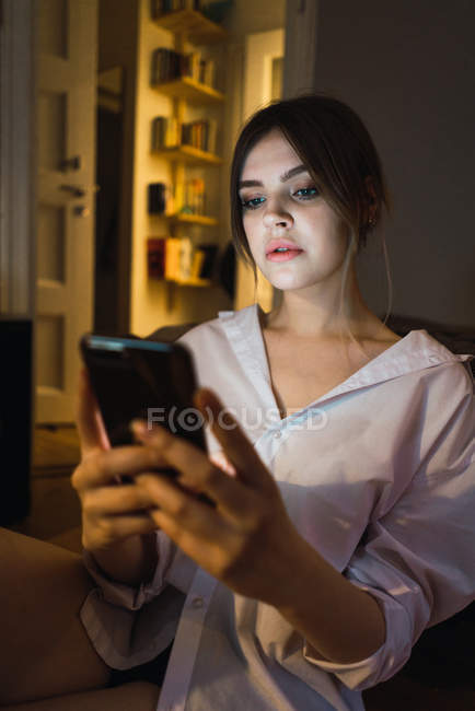 Retrato de una mujer sentada en el suelo y usando un smartphone - foto de stock