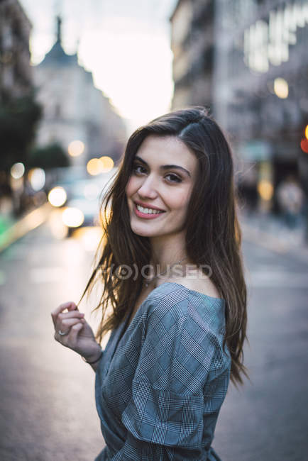 Junge brünette Frau läuft auf der städtischen Straße und schaut über die Schulter in die Kamera — Stockfoto