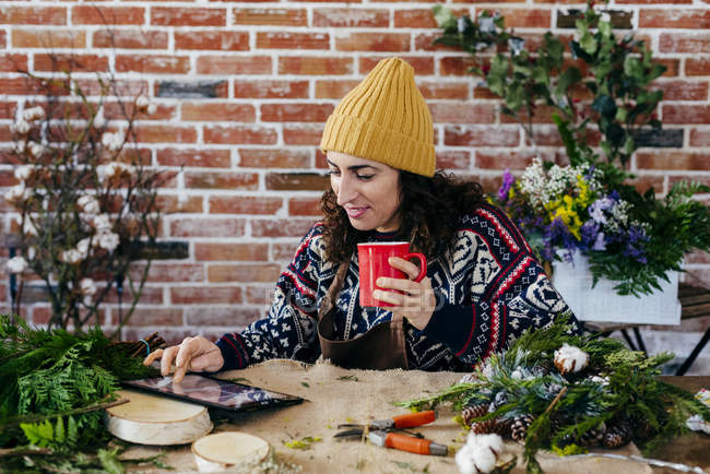 Портрет женщины, пьющей кофе и использующей планшет за столом в цветочном ателье — стоковое фото