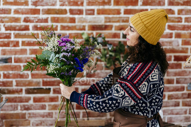 Side view of florist composing bouquet on background of loft brick wall — Stock Photo
