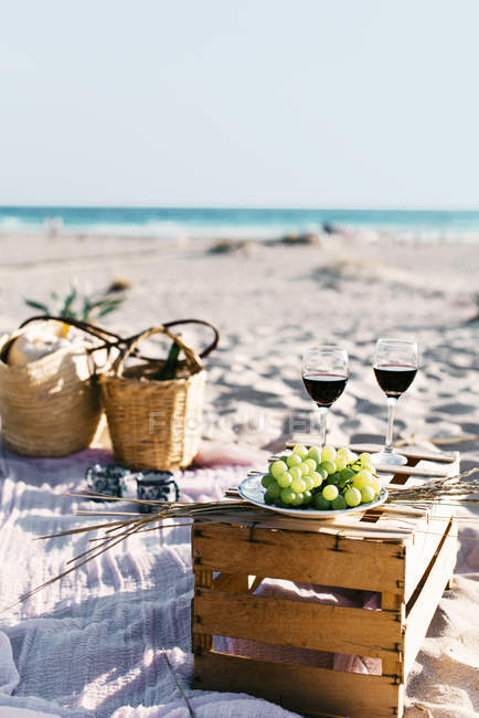Vista idilliaca di bicchieri da vino e uva in gabbia in spiaggia — Foto stock