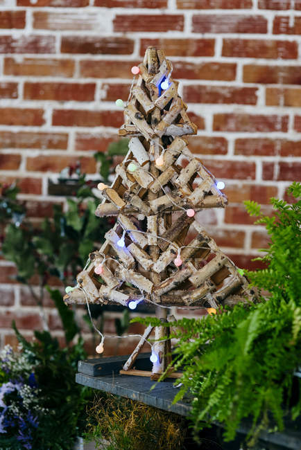 Vue rapprochée de l'arbre de Noël fabriqué à partir de poteaux en bois et décoré de lumières colorées . — Photo de stock