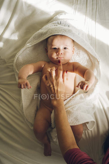 Crop hand touching chin of infant baby lying on towels and looking at camera. — Stock Photo