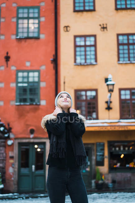 Вид спереди молодой женщины, позирующей на зимней улице и смотрящей вверх — стоковое фото
