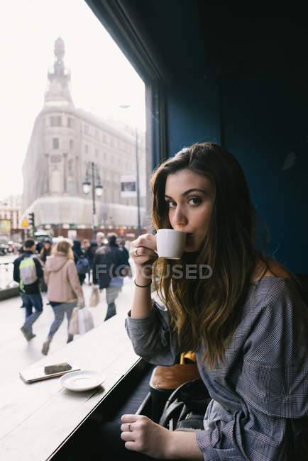 Retrato de mulher morena bebendo café pela janela no café — Fotografia de Stock