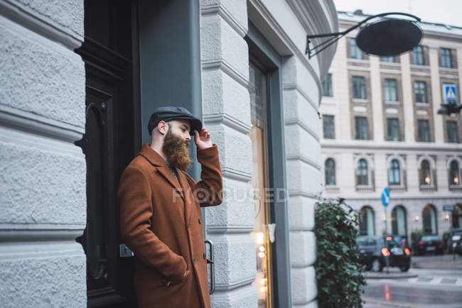 Продуманий стильний бородатий чоловік стоїть у дверях і одягає шапку — стокове фото