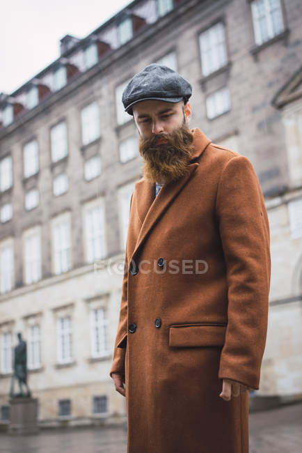 Portrait of bearded man in coat posing at street and looking down — Stock Photo