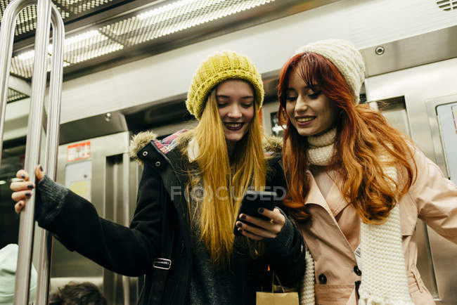 Vista de ángulo alto de dos chicas alegres usando el teléfono en el metro - foto de stock