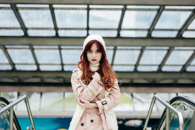 Portrait de jeune femme rousse debout dans le centre commercial et regardant la caméra — Photo de stock