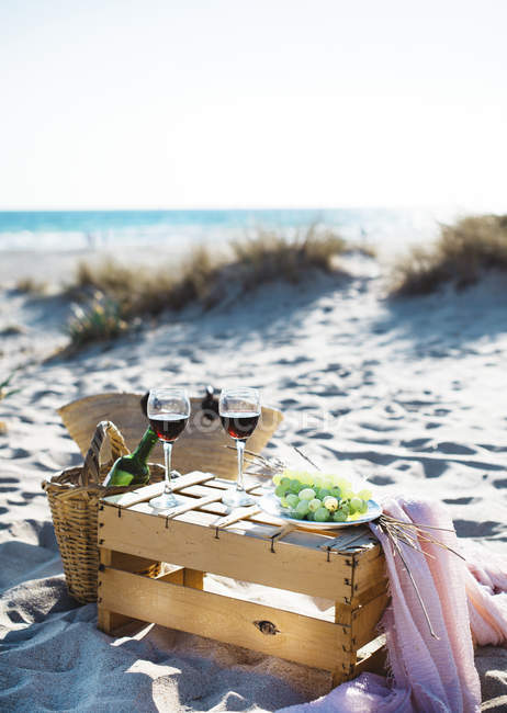 Натюрморт окулярів з вином і тарілкою з білим виноградом, що стоїть на дерев'яній ящику на пляжі . — стокове фото