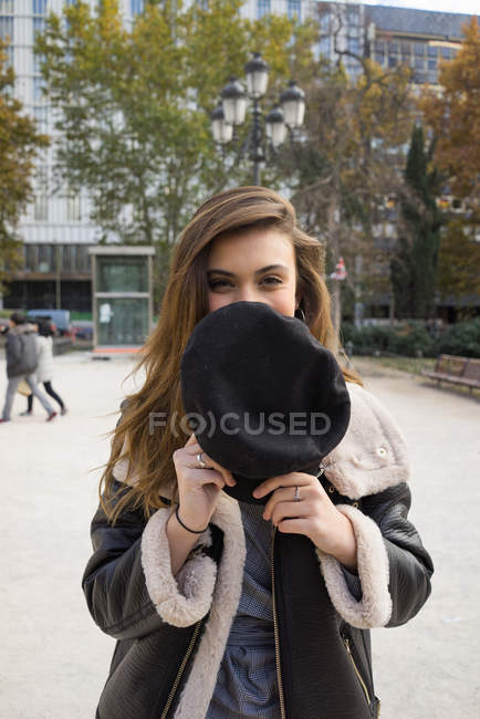 Porträt eines brünetten Mädchens, das Lächeln mit Mütze versteckt und in die Kamera blickt — Stockfoto