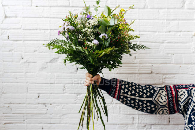Crop mano n maglia maglione tenendo bouquet su muro di mattoni bianchi — Foto stock