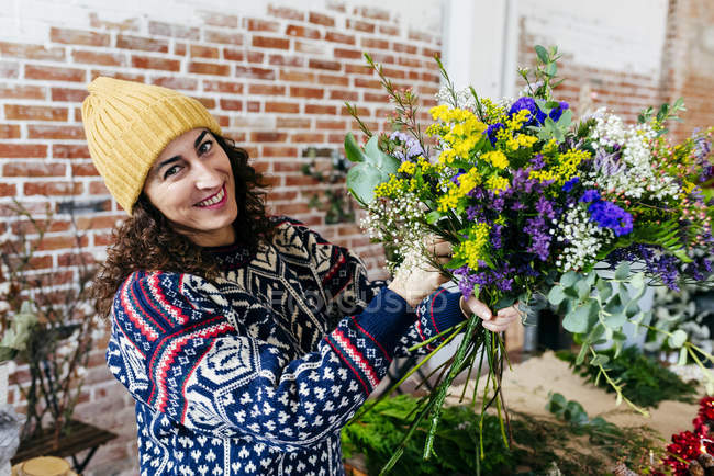 Portrait of smiling woman in jumper and hat making beautiful bouquet and looking at camera. — Stock Photo