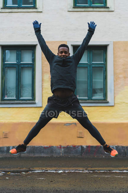 Portrait of man widely outstretching legs and arms while jumping on street — Stock Photo