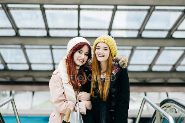 Pretty young women hugging in mall and looking at camera — Stock Photo
