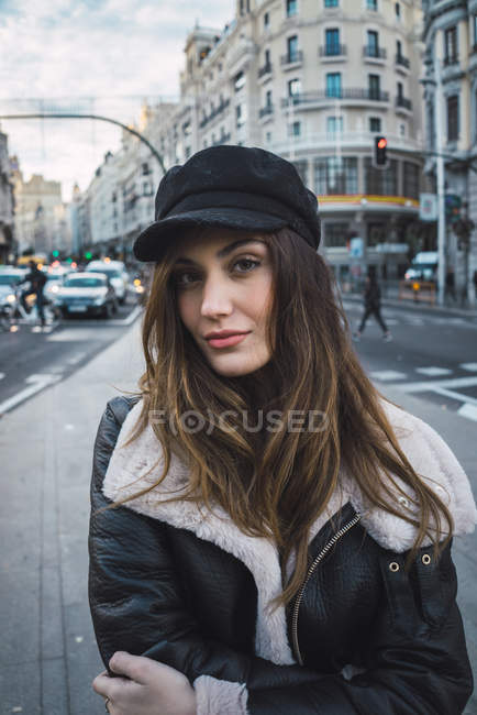 Porträt einer brünetten Frau mit stylischer Mütze, die auf der Straße in die Kamera schaut — Stockfoto