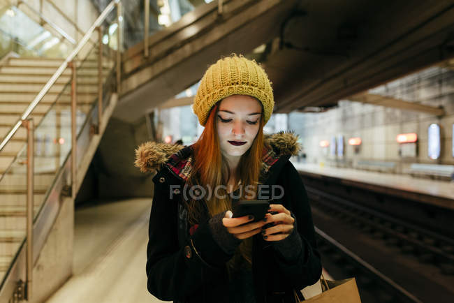 Portrait of young woman standing in subway and using smartphone — Stock Photo
