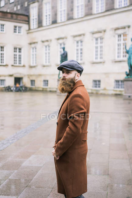 Homem barbudo vestindo casaco e boné andando na cidade — Fotografia de Stock