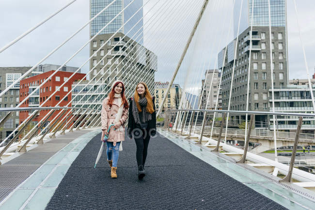 Вид спереди двух подруг, идущих по городскому мосту — стоковое фото