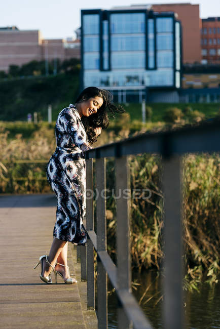 Вид збоку жінки в красивій сукні позує на мосту в міському парку — стокове фото