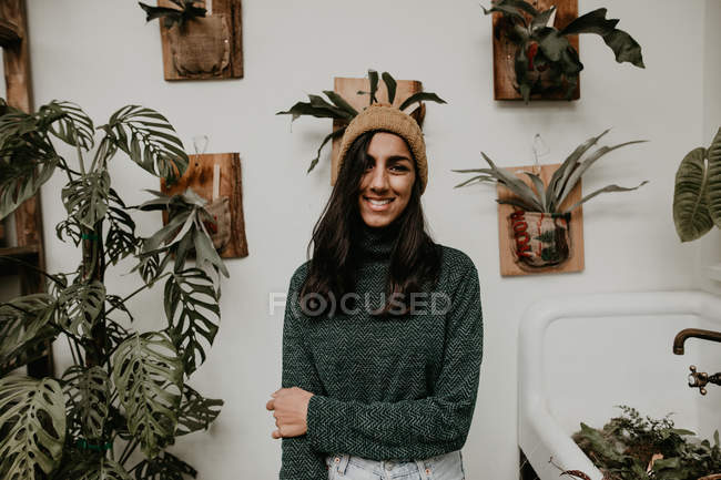 Retrato de mulher sorridente em pé no fundo da parede com plantas em vaso — Fotografia de Stock