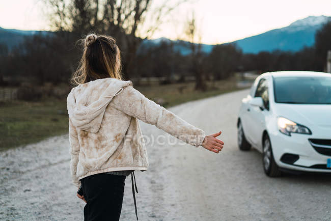 Rear view of girl gesturing while hitchhiking on remote road — Stock Photo