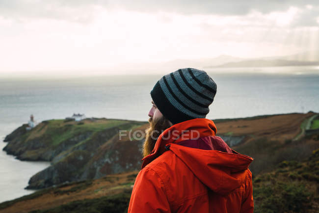 Side view of bearded man standing at coastal hills and admiring seascape — Stock Photo
