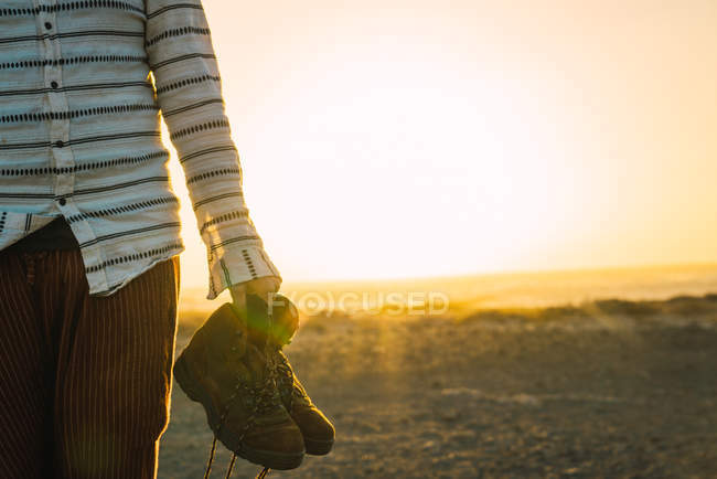 Crop male carrying boots in hand and walking in sunlit sand valley — Stock Photo