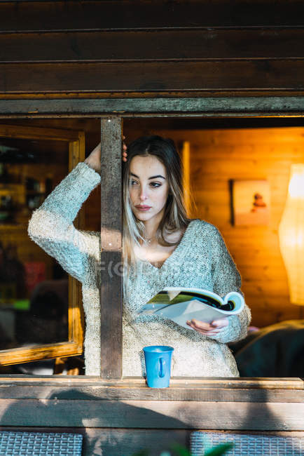 Retrato de mulher casual tomando café e segurando livro no chalé — Fotografia de Stock