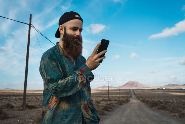 Portrait of bearded man using smartphone on road in countryside — Stock Photo