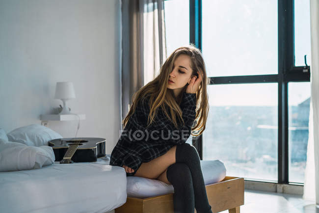 Portrait of stylish young girl sitting on bed with guitar — Stock Photo