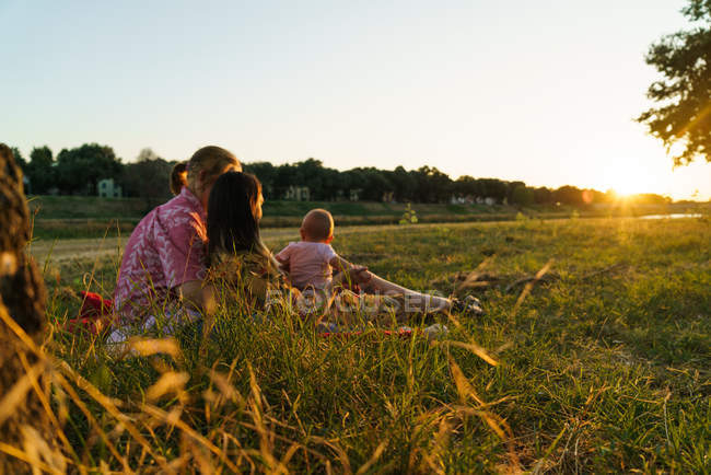 Seitenansicht einer glücklichen lesbischen Familie mit Kind auf der sonnenbeschienenen Parkwiese — Stockfoto