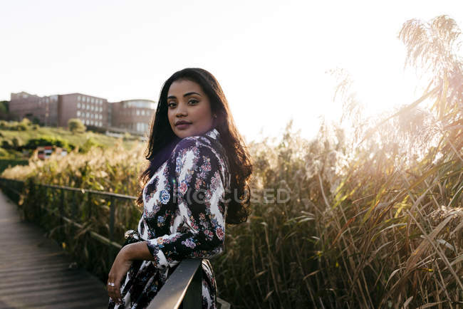 Portrait of woman in beautiful dress leaning on bridge handrail and looking over shoulder at camera — Stock Photo