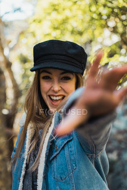 Portrait of laughing woman in cap outstretching hand looking at camera on nature. — Stock Photo