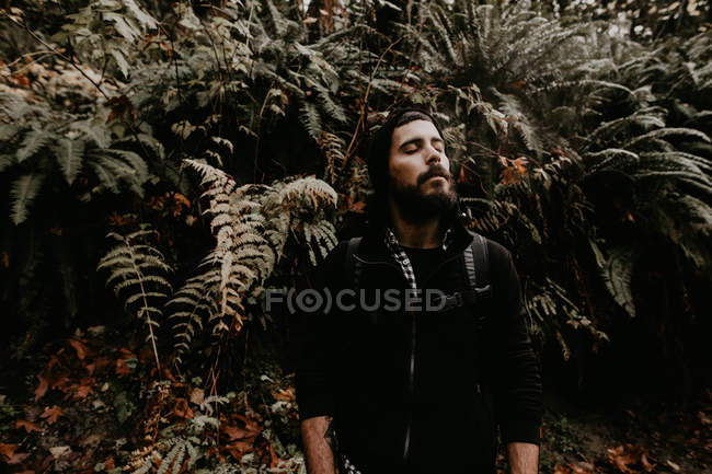 Portrait of tourist man standing and relaxing with eyes closed in forest. — Stock Photo