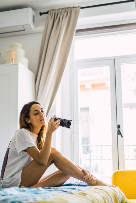 Вид збоку жінка, сидячи на ліжку у себе вдома і беручи розстріляний з камерою — стокове фото