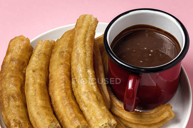Typical Spanish churros with hot chocolate sauce on pink — Stock Photo