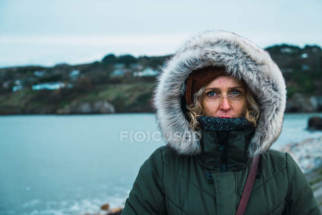 Портрет туристичної жінки в теплому одязі, дивлячись на камеру на тлі пагорбів і моря . — стокове фото