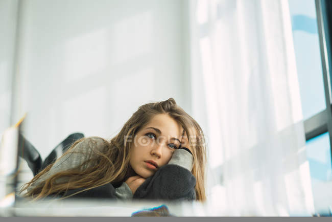 Blonde woman in sweater cuddling in bed and looking away — Stock Photo