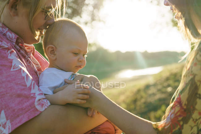 Cultiver couple lesbien avec enfant sur les mains au parc le soir d'été — Photo de stock