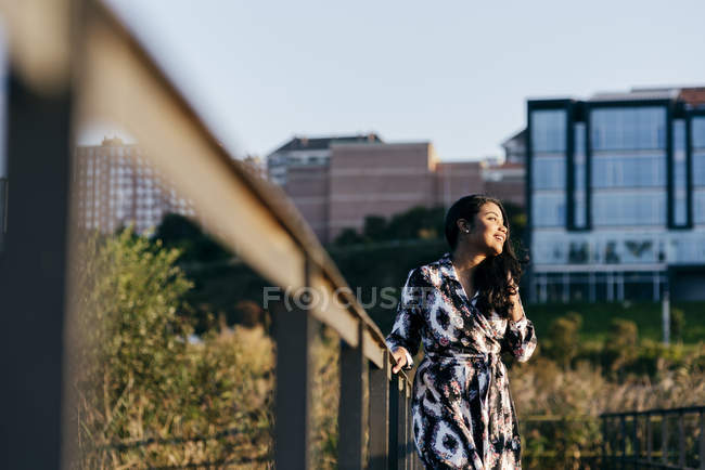 Retrato de mulher em belo vestido segurando corrimão e olhando para o parque da cidade — Fotografia de Stock