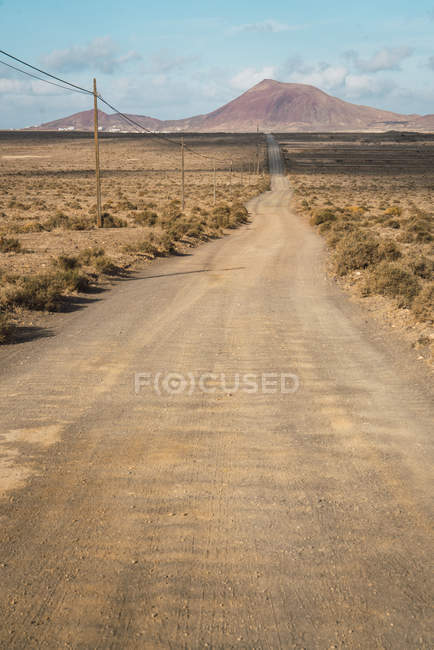 Перспективный вид на сельскую дорогу в горы и засушливое поле в сельской местности — стоковое фото