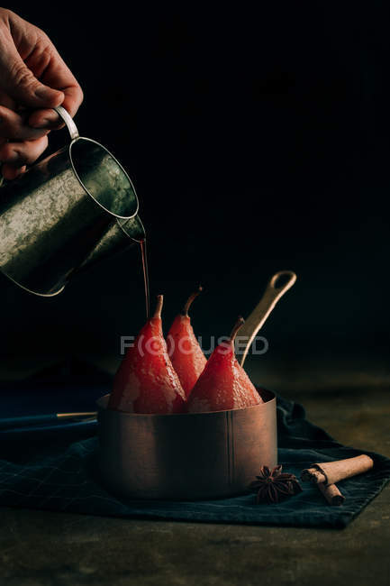 Mão de colheita derramando escalfado em peras de vinho tinto com canela e especiarias — Fotografia de Stock
